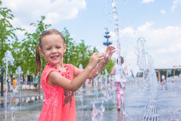 Petite fille heureuse s'amuser dans la fontaine de la rue à une journée chaude et ensoleillée