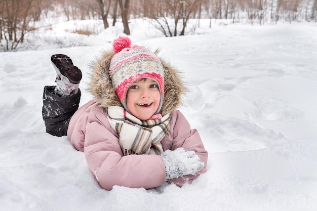 La petite fille heureuse se trouve dans la neige dehors en hiver