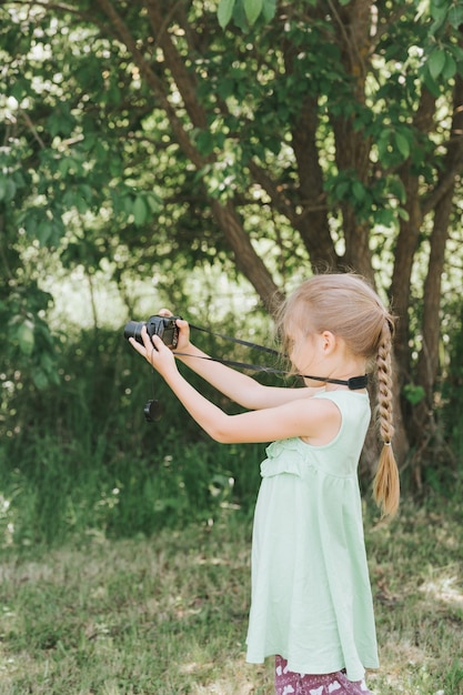 Une petite fille heureuse de sept ans photographie un paysage naturel d'été avec un appareil photo en utilisant la vue en direct. les enfants adoptent les loisirs de leurs parents. éducation des enfants d'été en vacances