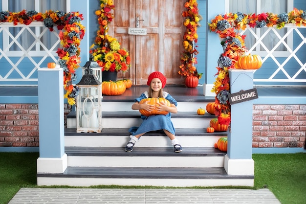 Petite fille heureuse tenant une citrouille assise sur le porche de la maison à l'Halloween.