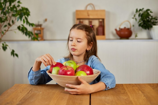 Une petite fille heureuse tient un bol avec des fruits dans la cuisine à la maison un en-cas sain pour un enfant Des aliments sains à la maison aiment les fruits et les vitamines