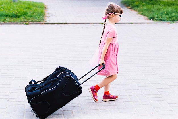Photo une petite fille heureuse tirant une valise sur roues le long d'une rue de la ville voyage de vacances