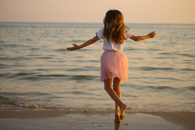 Une petite fille heureuse tourne et danse sur la plage par une journée ensoleillée.