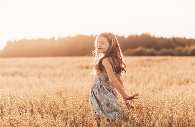 Une petite fille heureuse traverse un champ de blé en été par une journée ensoleillée. Heure d'été. Vacances d'été. Enfance heureuse. Émotions positives et énergie