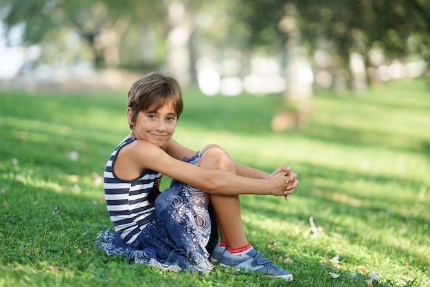 Petite fille de huit ans assise sur l'herbe en plein air.