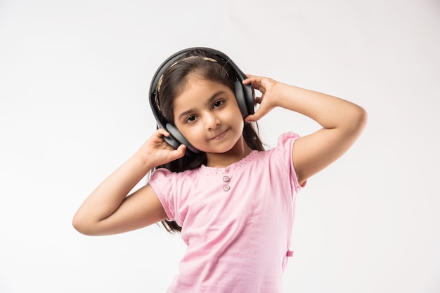 Petite fille indienne ou asiatique mignonne écoutant la musique sur des écouteurs sans fil d'isolement sur le blanc