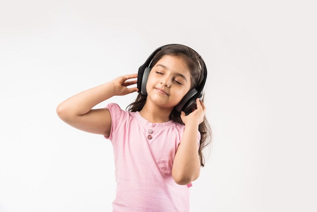 Petite fille indienne ou asiatique mignonne écoutant la musique sur des écouteurs sans fil d'isolement sur le blanc