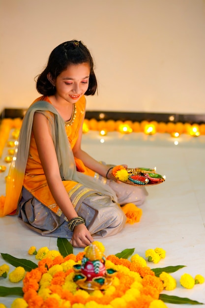 Petite fille indienne mignonne faisant la décoration avec la fleur et la lampe à huile pour le festival de diwali à la maison