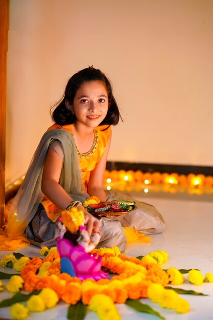 Petite fille indienne mignonne faisant la décoration avec la fleur et la lampe à huile pour le festival de diwali à la maison