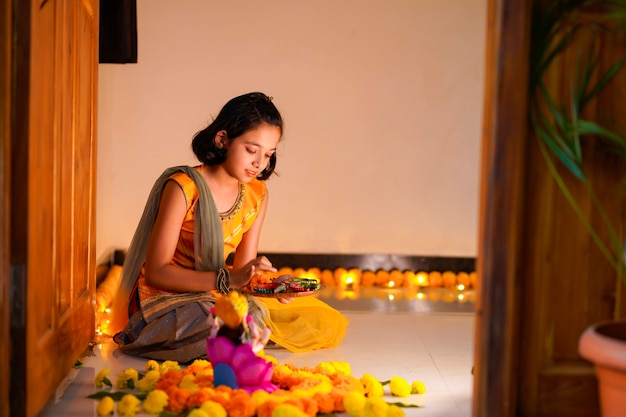 Petite fille indienne mignonne faisant la décoration avec la fleur et la lampe à huile pour le festival de diwali à la maison