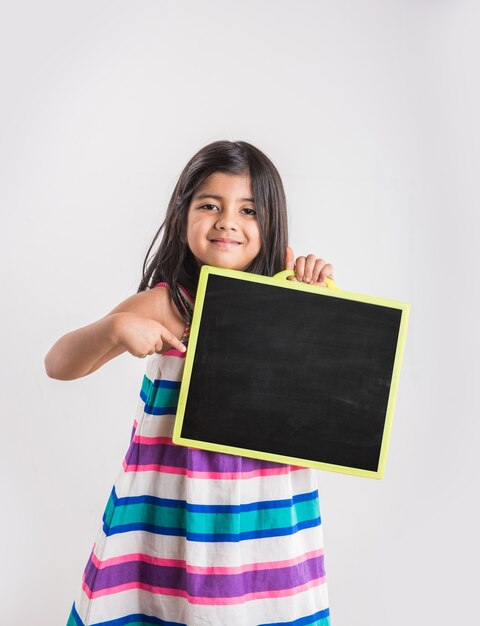 Petite fille indienne mignonne montrant le blanc ou l'abc écrit sur l'ardoise noire d'école, d'isolement au-dessus du fond blanc