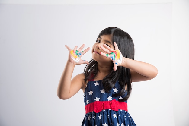 Petite fille indienne mignonne montrant ses mains colorées ou l'impression de paume ou la peinture ou jouant le festival de holi avec des couleurs, d'isolement au-dessus du fond blanc