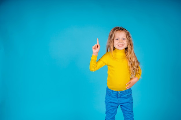 Une petite fille isolée sur fond bleu montre le geste avec le doigt vers le haut