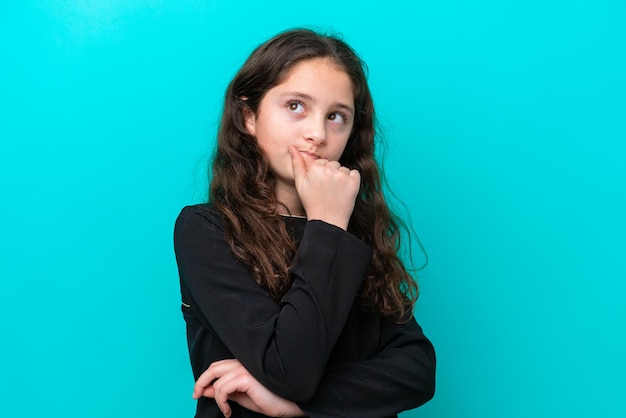 Petite fille isolée sur fond bleu pensant à une idée tout en levant les yeux