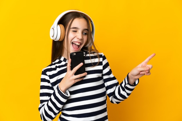 Petite fille isolée sur fond jaune, écoutant de la musique avec un mobile et chantant