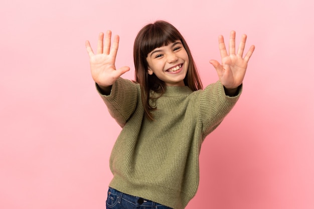 Petite fille isolée sur fond rose comptant dix avec les doigts