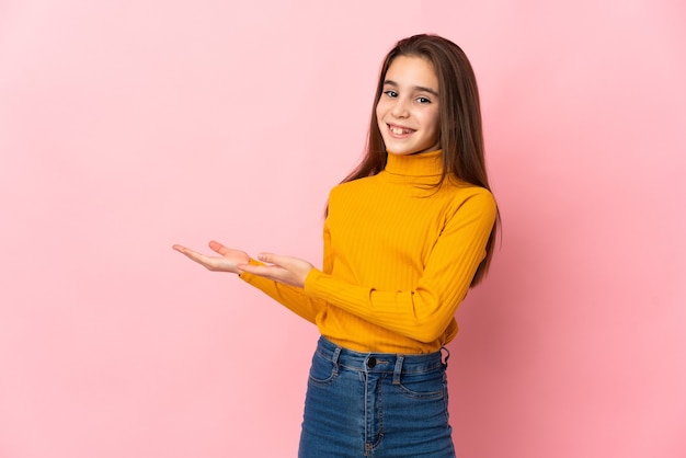 Petite fille isolée sur fond rose étendant les mains sur le côté pour inviter à venir