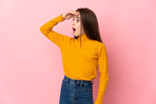 Petite fille isolée sur fond rose faisant un geste surprise en regardant sur le côté