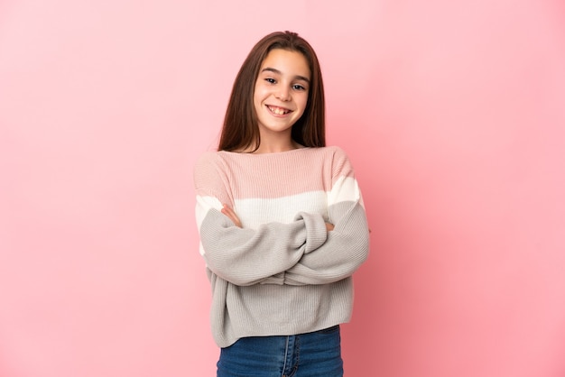 Petite fille isolée sur fond rose en gardant les bras croisés en position frontale