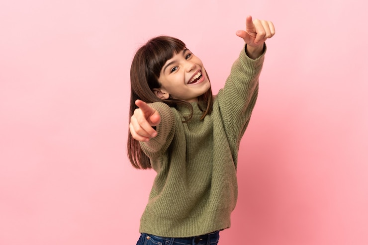 Photo petite fille isolée sur fond rose pointant vers l'avant avec une expression heureuse