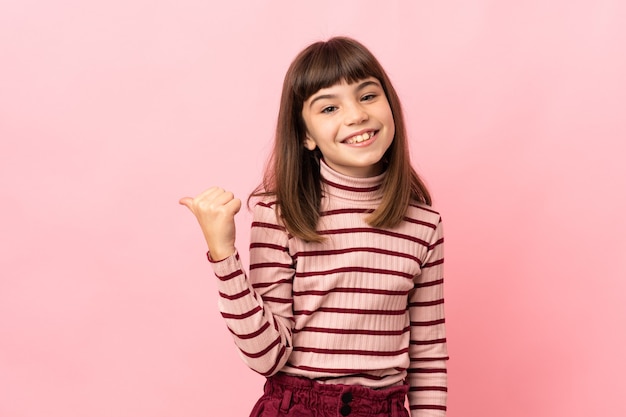 Petite fille isolée sur fond rose pointant vers le côté pour présenter un produit