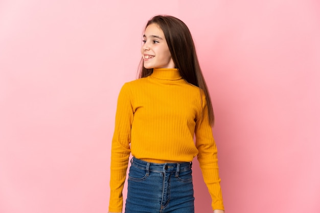 Petite fille isolée sur fond rose regardant sur le côté et souriant