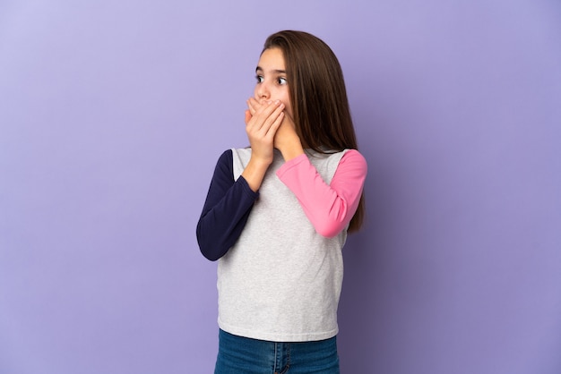 Petite fille isolée sur fond violet couvrant la bouche et regardant sur le côté