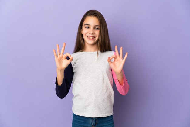 Petite fille isolée sur fond violet montrant signe ok avec deux mains