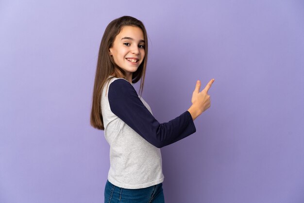 Petite fille isolée sur fond violet pointant vers l'arrière