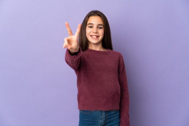 Petite fille isolée sur fond violet souriant et montrant le signe de la victoire