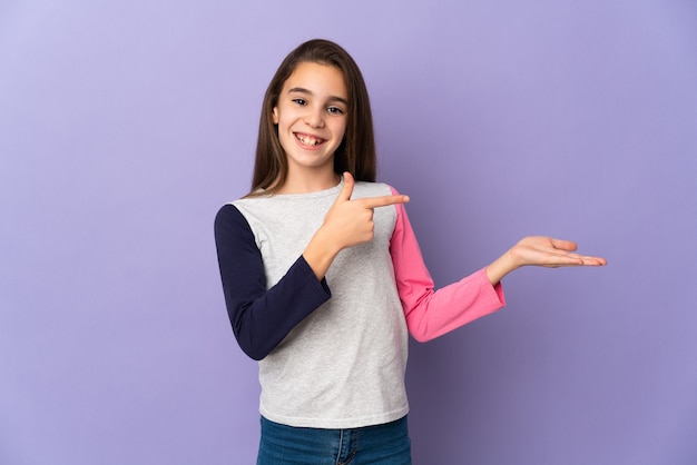 Petite fille isolée sur fond violet tenant copyspace imaginaire sur la paume pour insérer une annonce