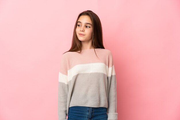 Petite fille isolée sur un mur rose ayant des doutes tout en regardant côté