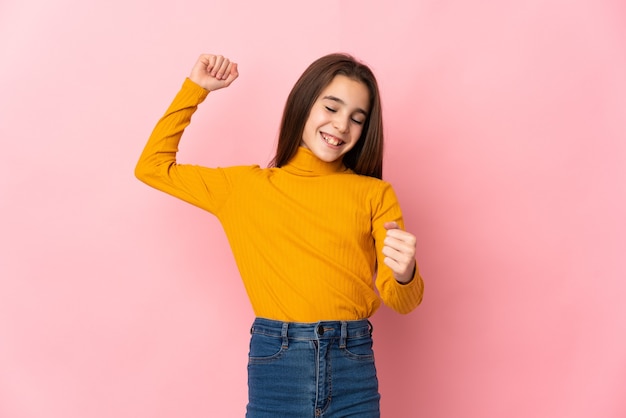 Petite fille isolée sur un mur rose célébrant une victoire