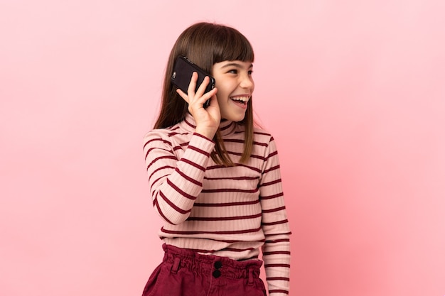 Petite fille isolée sur un mur rose en gardant une conversation avec le téléphone mobile
