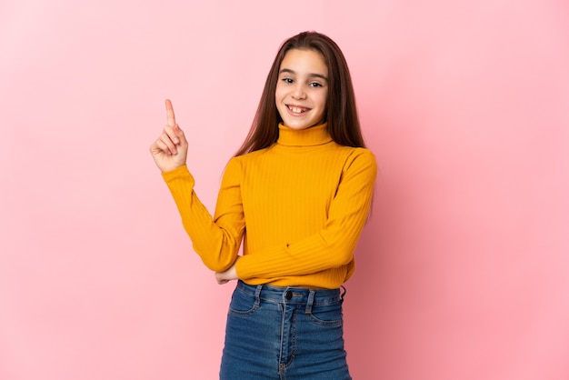 Petite fille isolée sur un mur rose heureux et pointant vers le haut