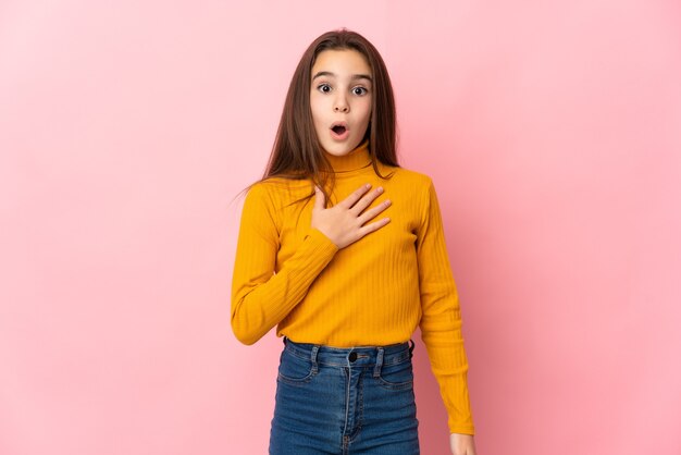 Petite fille isolée sur un mur rose surpris et choqué tout en regardant à droite