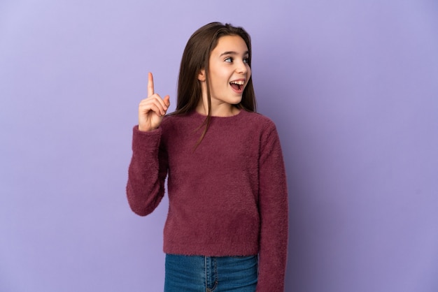 Petite fille isolée sur un mur violet dans l'intention de réaliser la solution tout en levant un doigt
