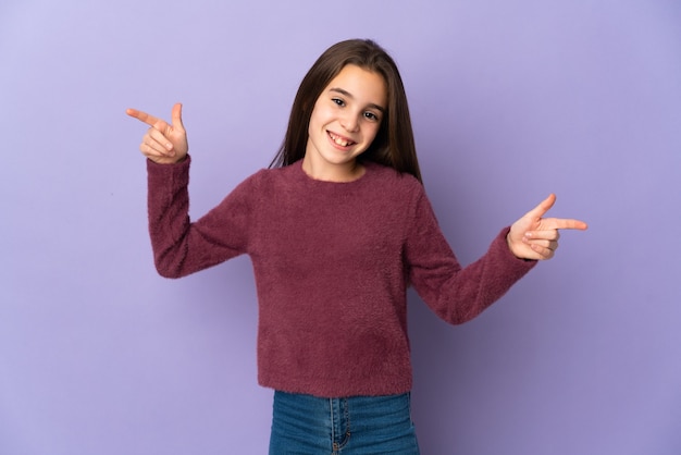 Petite fille isolée sur le mur violet pointant le doigt vers les latéraux et heureux