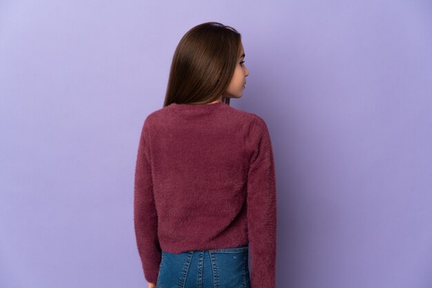 Petite fille isolée sur un mur violet en position arrière et à côté