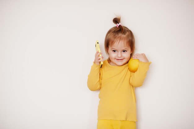 Petite fille en jaune avec citron et téléphone portable, fond isolé.