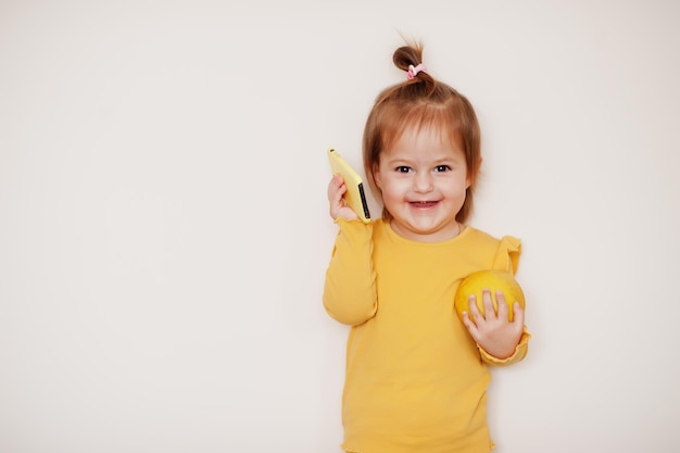 Petite fille en jaune avec citron et téléphone portable, fond isolé.