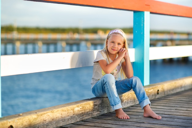 Une petite fille en jeans et un T-shirt est assise sur une jetée près de la mer Baltique.Palanga, Lituanie