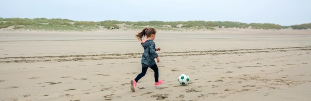 Petite fille jouant au football sur la plage en automne