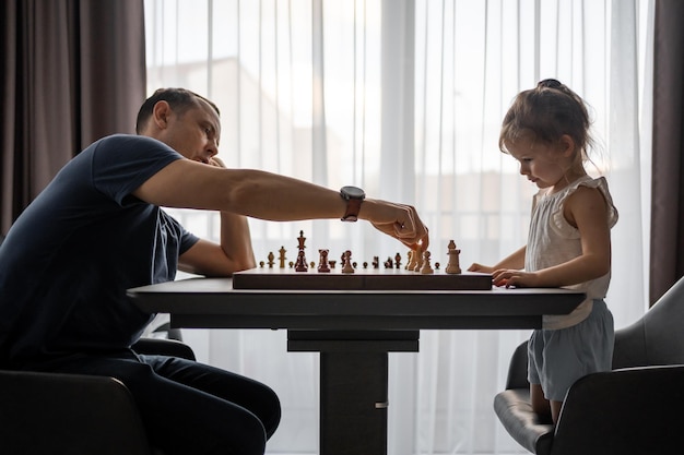 Petite fille jouant aux échecs avec son père à la table dans la cuisine à domicile le concept de la petite enfance d