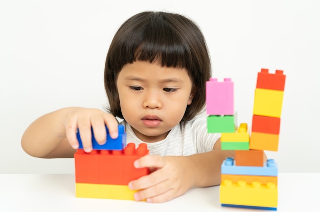 Petite fille jouant avec des blocs de jouets colorés sur blanc, les enfants jouent avec des jouets éducatifs