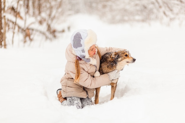 Petite fille jouant avec un chien dans la forêt d'hiver. plaisir d'hiver