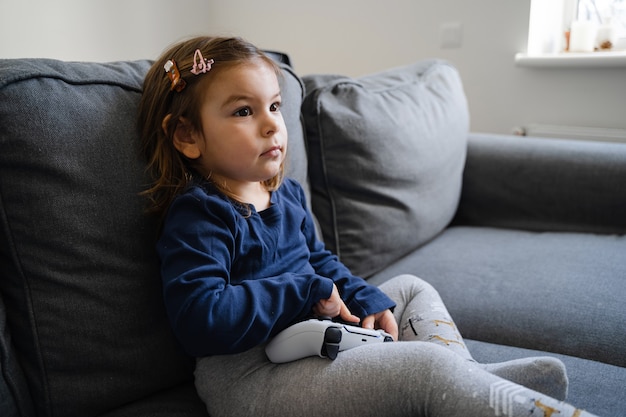 Petite fille jouant à la console de jeu vidéo à la maison dans le salon sur le canapé. Jeune gamer gamer.