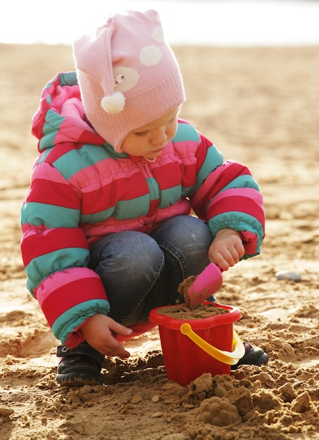 Petite fille jouant avec du sable à la plage d'automne