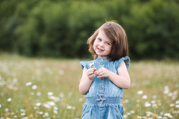 Petite fille jouant avec des fleurs posant dans le pré