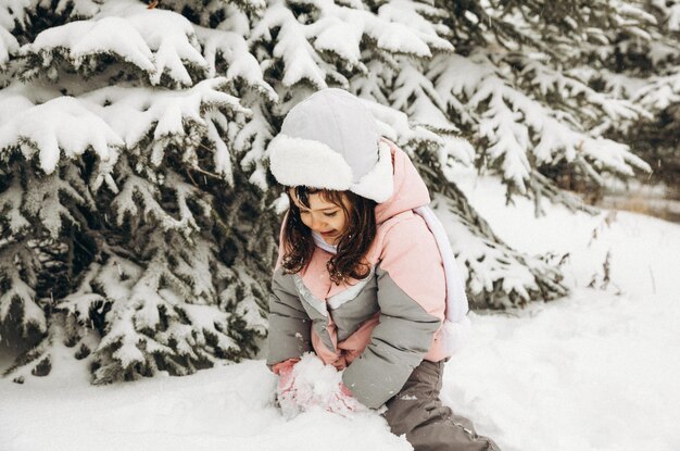 Petite fille jouant en hiver dans la forêt enneigée. Beau portrait d'enfant d'hiver. Enfant heureux, plaisirs d'hiver à l'extérieur.